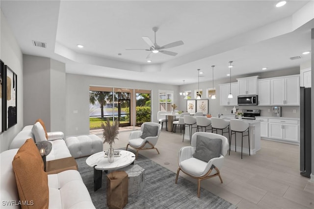 living room with a tray ceiling and ceiling fan with notable chandelier