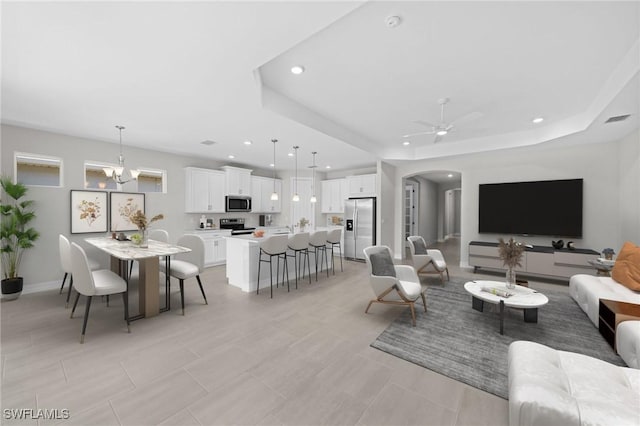 living room featuring ceiling fan with notable chandelier and a raised ceiling