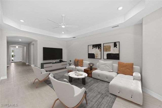 living room with ceiling fan and a raised ceiling