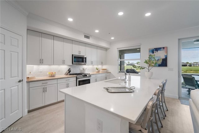 kitchen with sink, a kitchen island with sink, a breakfast bar, white cabinets, and appliances with stainless steel finishes