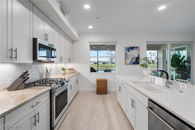 kitchen with decorative backsplash, appliances with stainless steel finishes, light wood-type flooring, sink, and white cabinetry