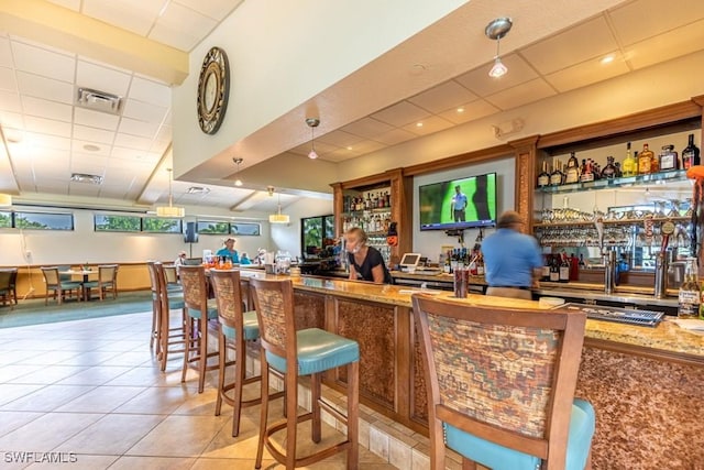 bar with light stone counters, light tile patterned flooring, and hanging light fixtures