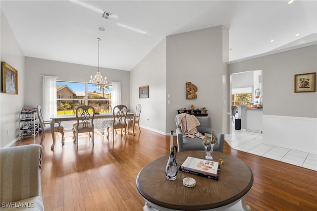 dining space with light wood-type flooring, high vaulted ceiling, and a notable chandelier