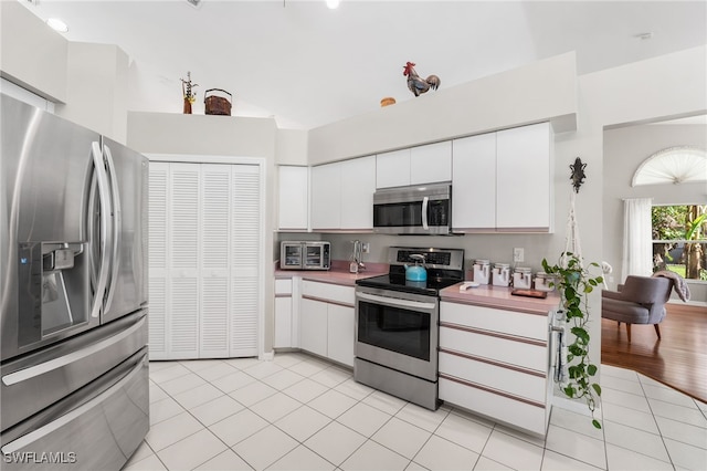 kitchen featuring white cabinetry, light tile patterned floors, stainless steel appliances, and a high ceiling