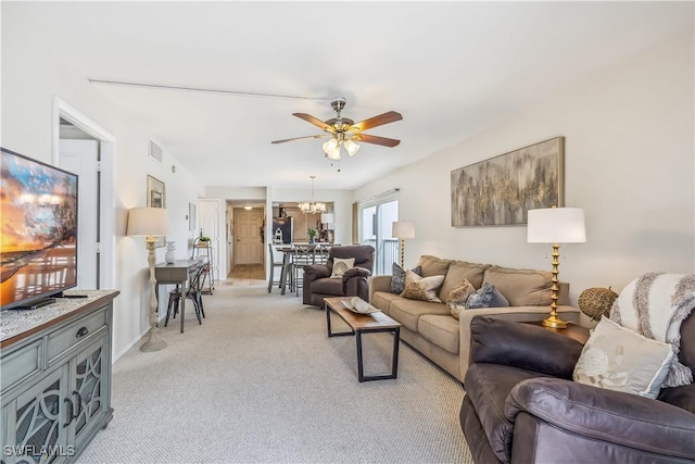 carpeted living room featuring ceiling fan with notable chandelier