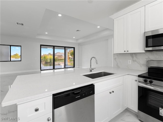 kitchen featuring kitchen peninsula, sink, appliances with stainless steel finishes, a tray ceiling, and white cabinetry