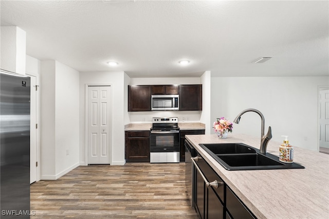 kitchen featuring sink, appliances with stainless steel finishes, dark brown cabinets, and light wood-type flooring