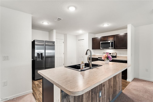 kitchen featuring sink, a kitchen island with sink, appliances with stainless steel finishes, a textured ceiling, and dark brown cabinets