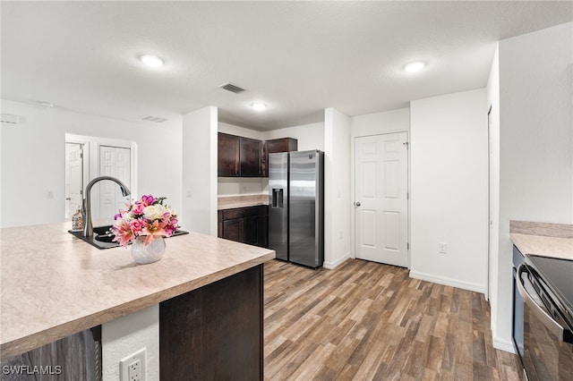 kitchen featuring electric range oven, dark brown cabinetry, stainless steel refrigerator with ice dispenser, wood-type flooring, and sink