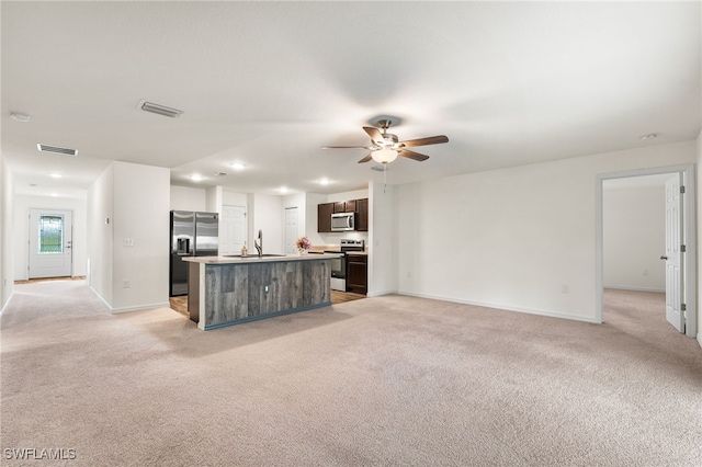 kitchen with light carpet, stainless steel appliances, dark brown cabinets, and an island with sink