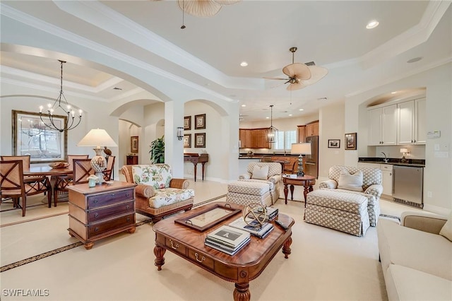 living room featuring a tray ceiling, crown molding, sink, and ceiling fan with notable chandelier