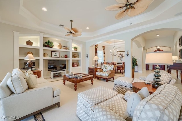 living room with ceiling fan with notable chandelier, a tray ceiling, built in features, and ornamental molding