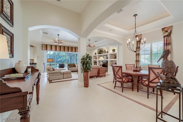 tiled dining space featuring built in shelves, ceiling fan with notable chandelier, a raised ceiling, and crown molding