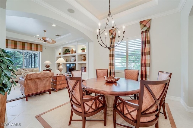 dining area with built in shelves, a raised ceiling, light tile patterned floors, ceiling fan with notable chandelier, and ornamental molding