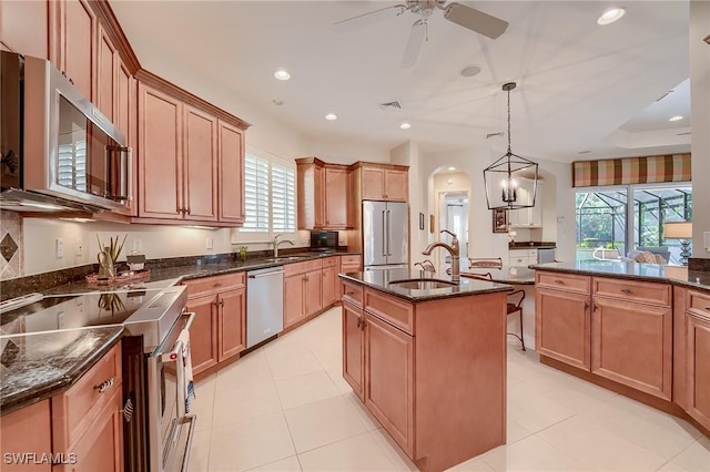 kitchen featuring high end appliances, ceiling fan with notable chandelier, sink, an island with sink, and decorative light fixtures