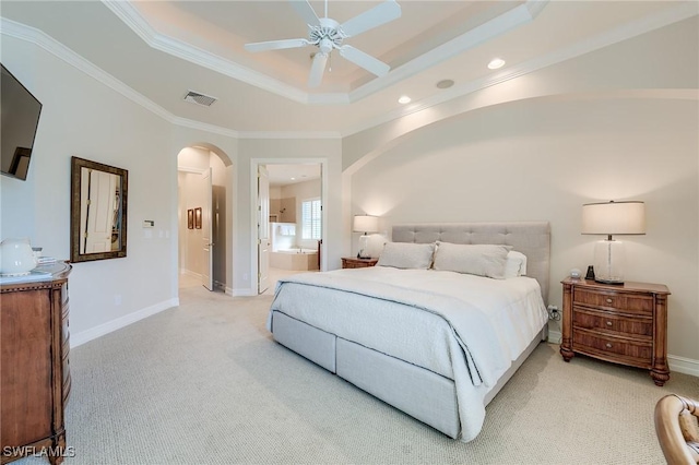 carpeted bedroom with ceiling fan, a raised ceiling, crown molding, and ensuite bath