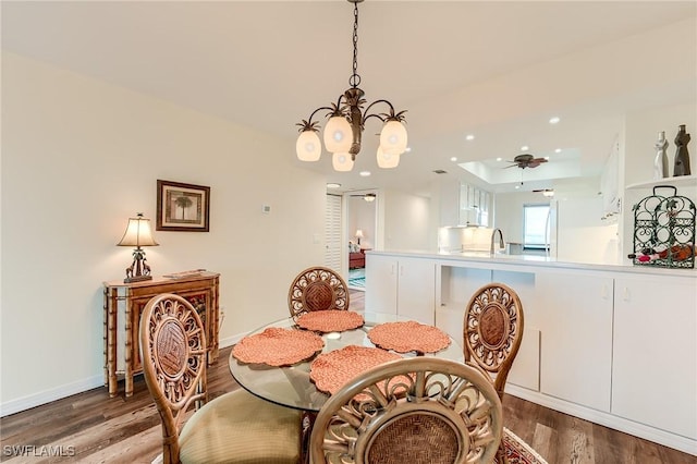 dining space featuring a tray ceiling, sink, hardwood / wood-style flooring, and a chandelier