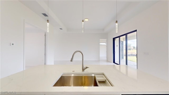 kitchen featuring light stone counters, sink, decorative light fixtures, and a raised ceiling