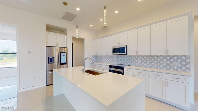 kitchen with sink, an island with sink, pendant lighting, stainless steel appliances, and white cabinets