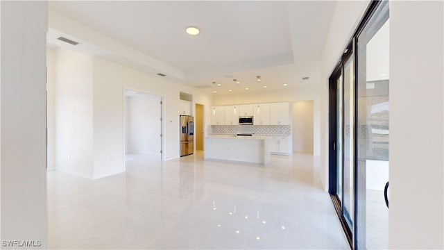 kitchen with a kitchen island, appliances with stainless steel finishes, white cabinetry, decorative backsplash, and a raised ceiling