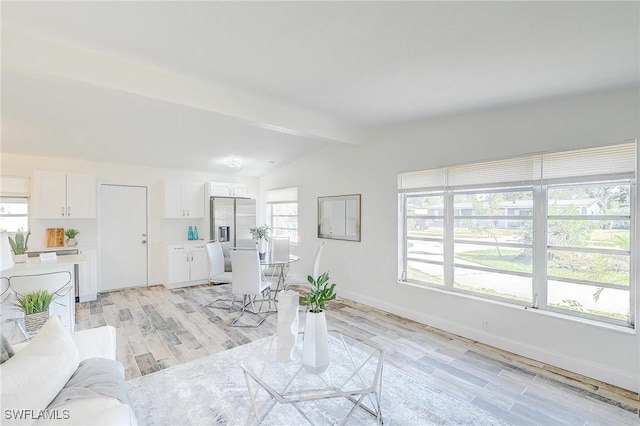 unfurnished living room featuring lofted ceiling with beams, a healthy amount of sunlight, and light hardwood / wood-style floors