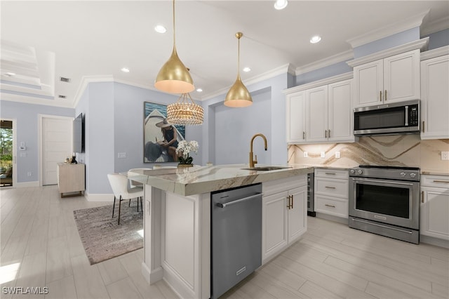 kitchen with sink, an island with sink, decorative backsplash, white cabinets, and appliances with stainless steel finishes