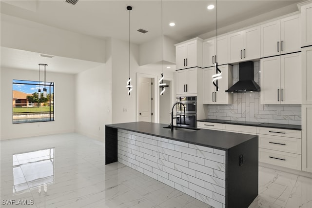 kitchen with a kitchen island with sink, white cabinetry, wall chimney exhaust hood, and hanging light fixtures