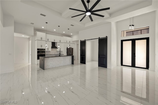 kitchen featuring a barn door, decorative light fixtures, an island with sink, white cabinetry, and range hood