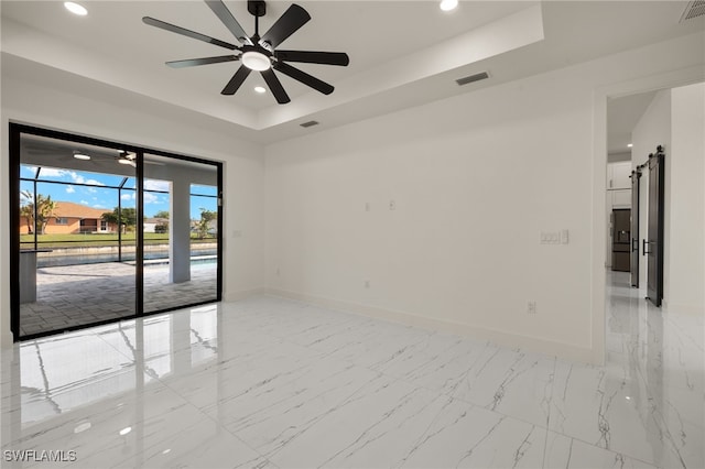 unfurnished room featuring ceiling fan, a barn door, and a tray ceiling