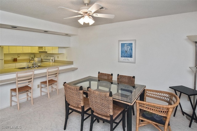 dining room with a textured ceiling, sink, built in desk, light colored carpet, and ceiling fan