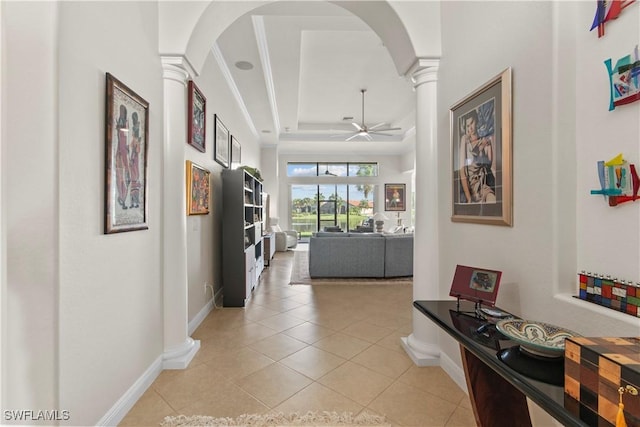 corridor with light tile patterned floors, ornamental molding, a tray ceiling, and decorative columns