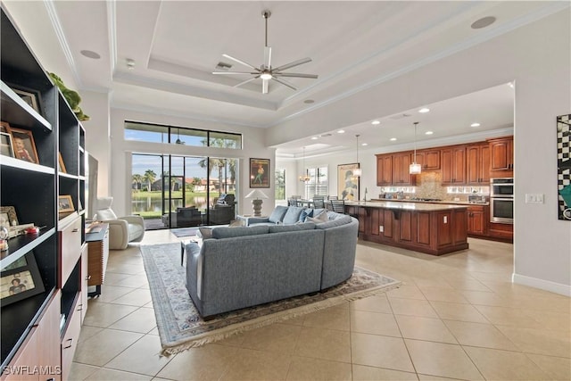 tiled living room with ceiling fan, sink, ornamental molding, and a raised ceiling