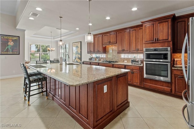 kitchen featuring crown molding, hanging light fixtures, light stone countertops, an island with sink, and light tile patterned flooring