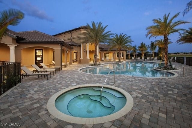 pool at dusk featuring a hot tub and a patio area