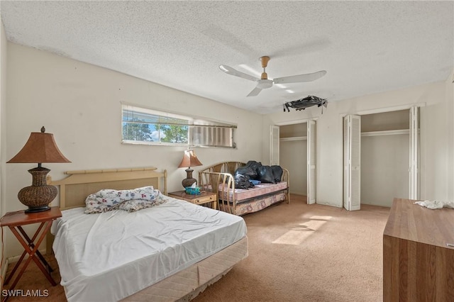 carpeted bedroom with ceiling fan, two closets, and a textured ceiling