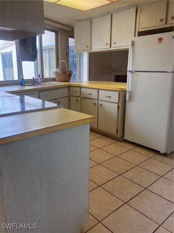 kitchen with black stovetop, white fridge, light tile patterned floors, and kitchen peninsula