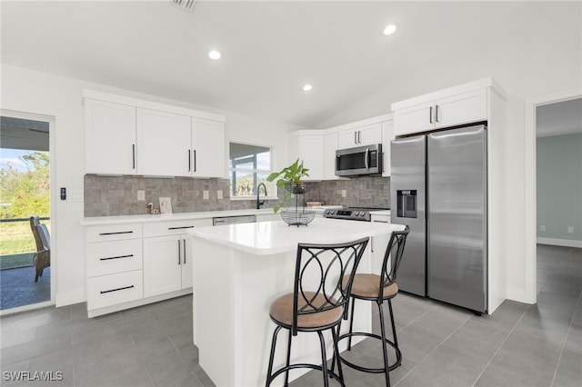 kitchen with a center island, a healthy amount of sunlight, lofted ceiling, white cabinets, and appliances with stainless steel finishes