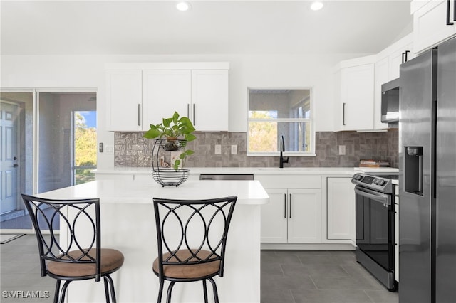 kitchen with a kitchen bar, backsplash, stainless steel appliances, sink, and white cabinets