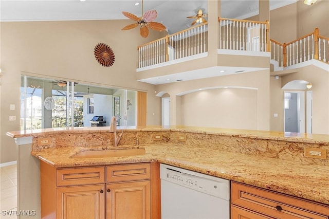 kitchen featuring light stone counters, white dishwasher, ceiling fan, sink, and a high ceiling