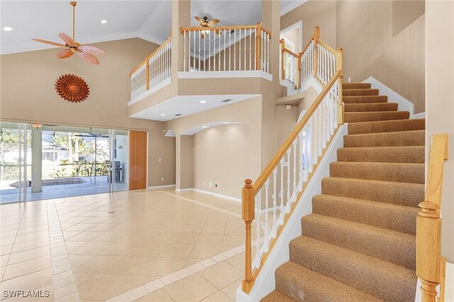 stairs with tile patterned flooring, ceiling fan, and a towering ceiling