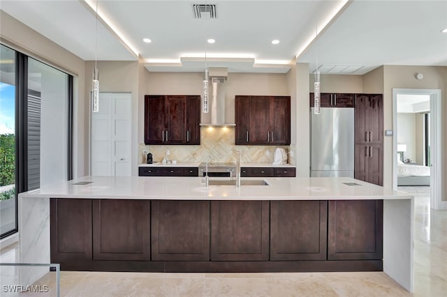 kitchen with pendant lighting, sink, wall chimney exhaust hood, stainless steel fridge, and decorative backsplash