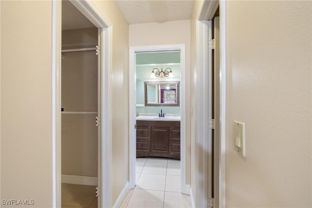 corridor with a textured ceiling, light tile patterned floors, and sink