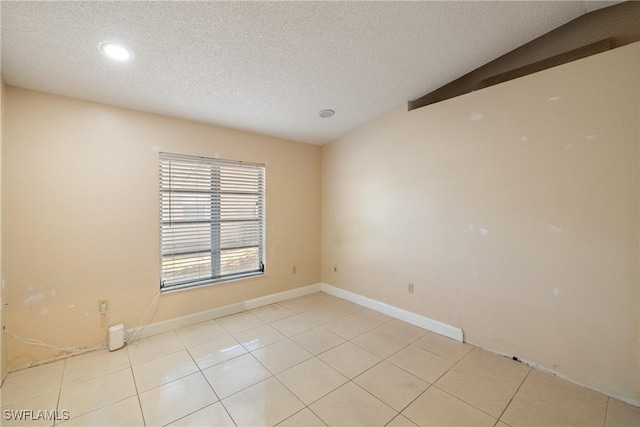 tiled empty room with a textured ceiling and vaulted ceiling