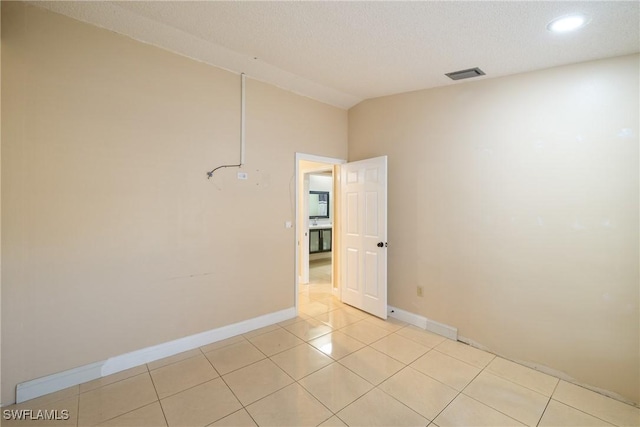 tiled empty room featuring a textured ceiling and lofted ceiling