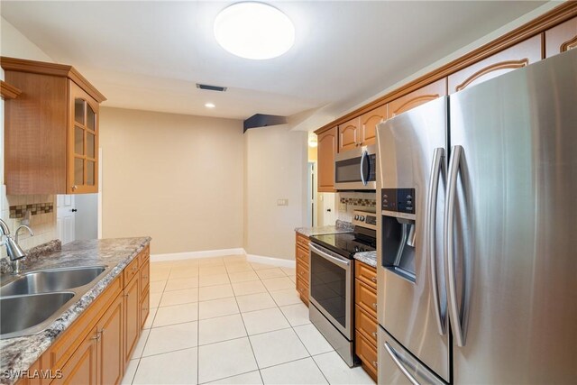 kitchen featuring light stone countertops, sink, light tile patterned floors, and stainless steel appliances