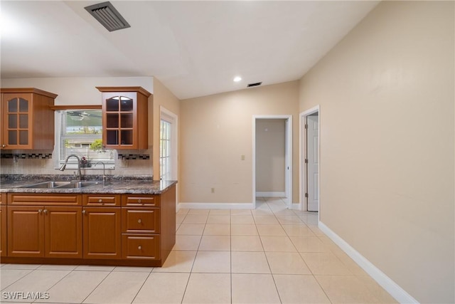 kitchen featuring sink, dark stone counters, lofted ceiling, decorative backsplash, and light tile patterned floors