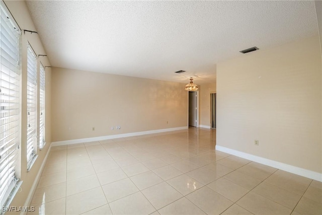 tiled empty room featuring a textured ceiling and a notable chandelier