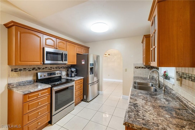 kitchen with dark stone counters, sink, decorative backsplash, light tile patterned floors, and stainless steel appliances