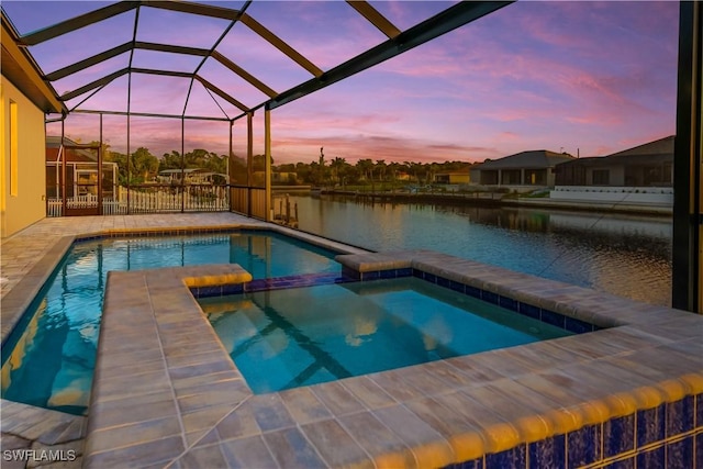 pool at dusk with glass enclosure, an in ground hot tub, a patio area, and a water view