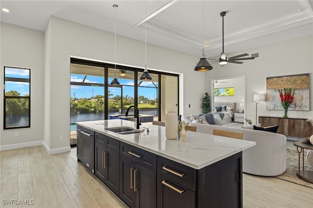 kitchen featuring ceiling fan, light stone countertops, an island with sink, decorative light fixtures, and a water view